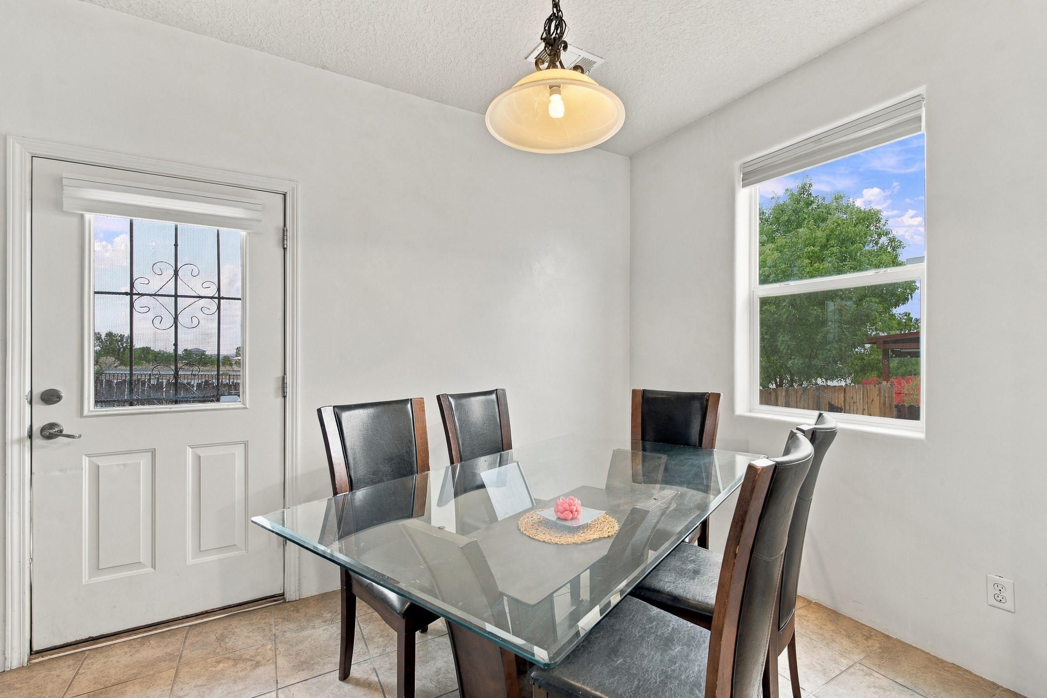Dining room with a glass-top table, dark chairs, and a large window overlooking trees.