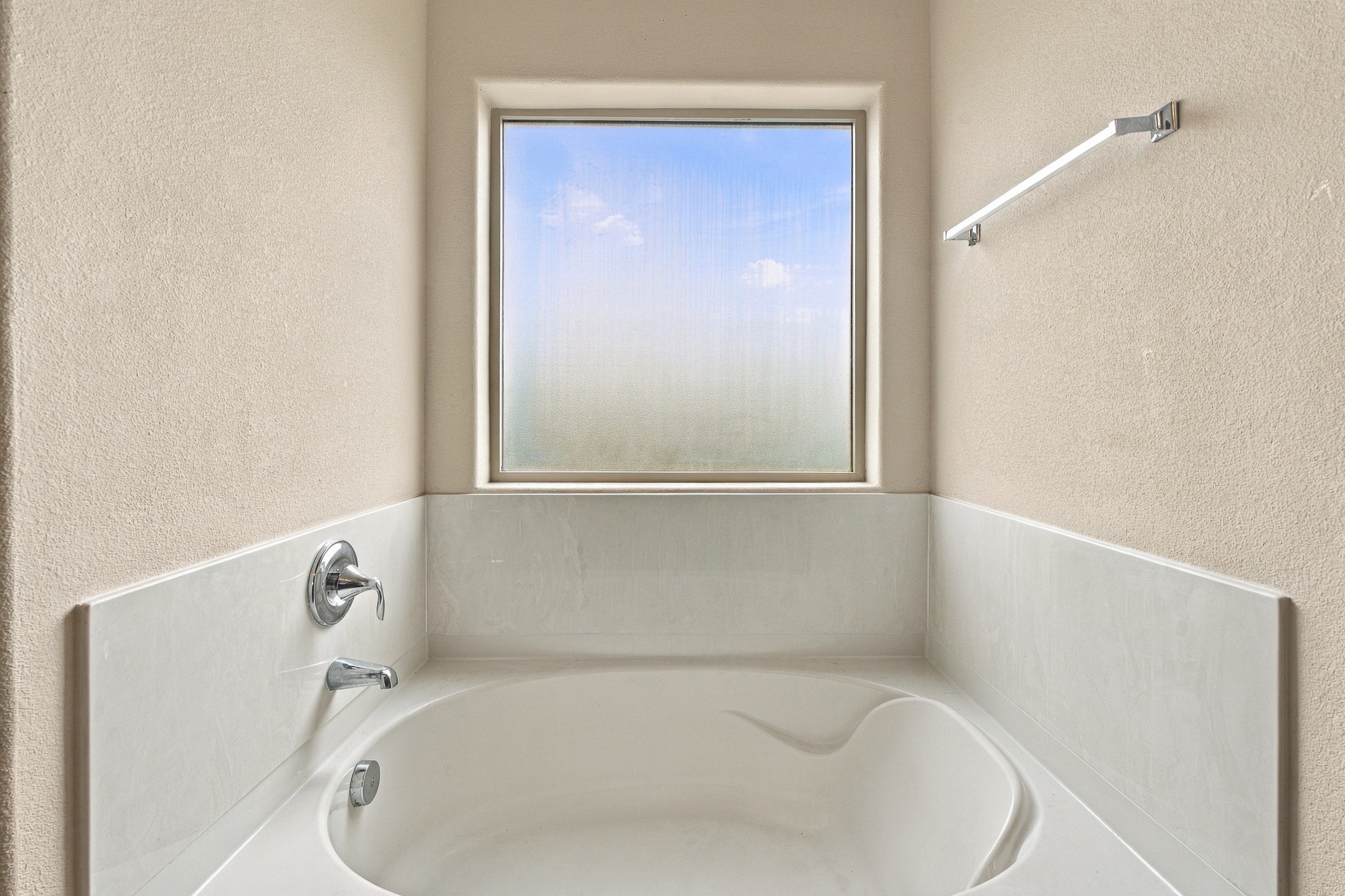 Built-in white soaking tub beneath a large window, with chrome fixtures and light tile surrounds.