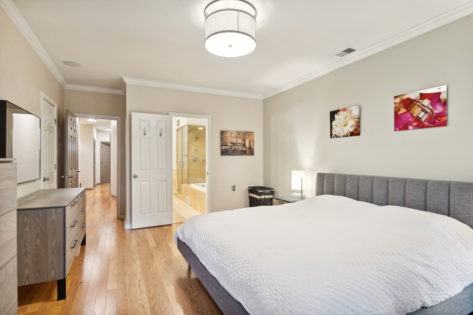 Bedroom with a large white bed and gray headboard, opening to a bathroom with a glass shower and tub.
