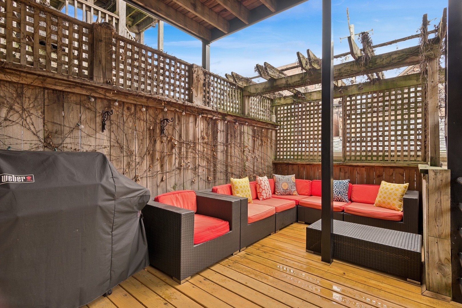 Covered wooden deck patio with coral-cushioned wicker seating, lattice screens, and a covered grill.