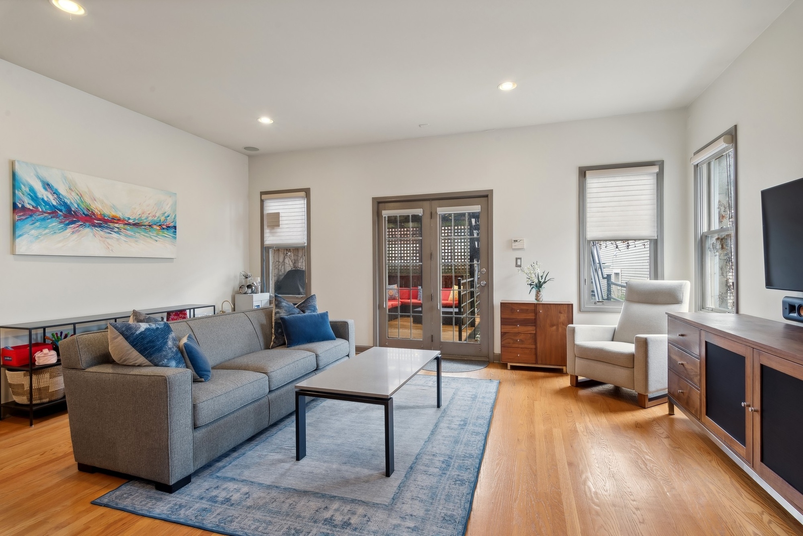 Living room with gray sofa, blue rug, hardwood floors, and French doors to a deck.