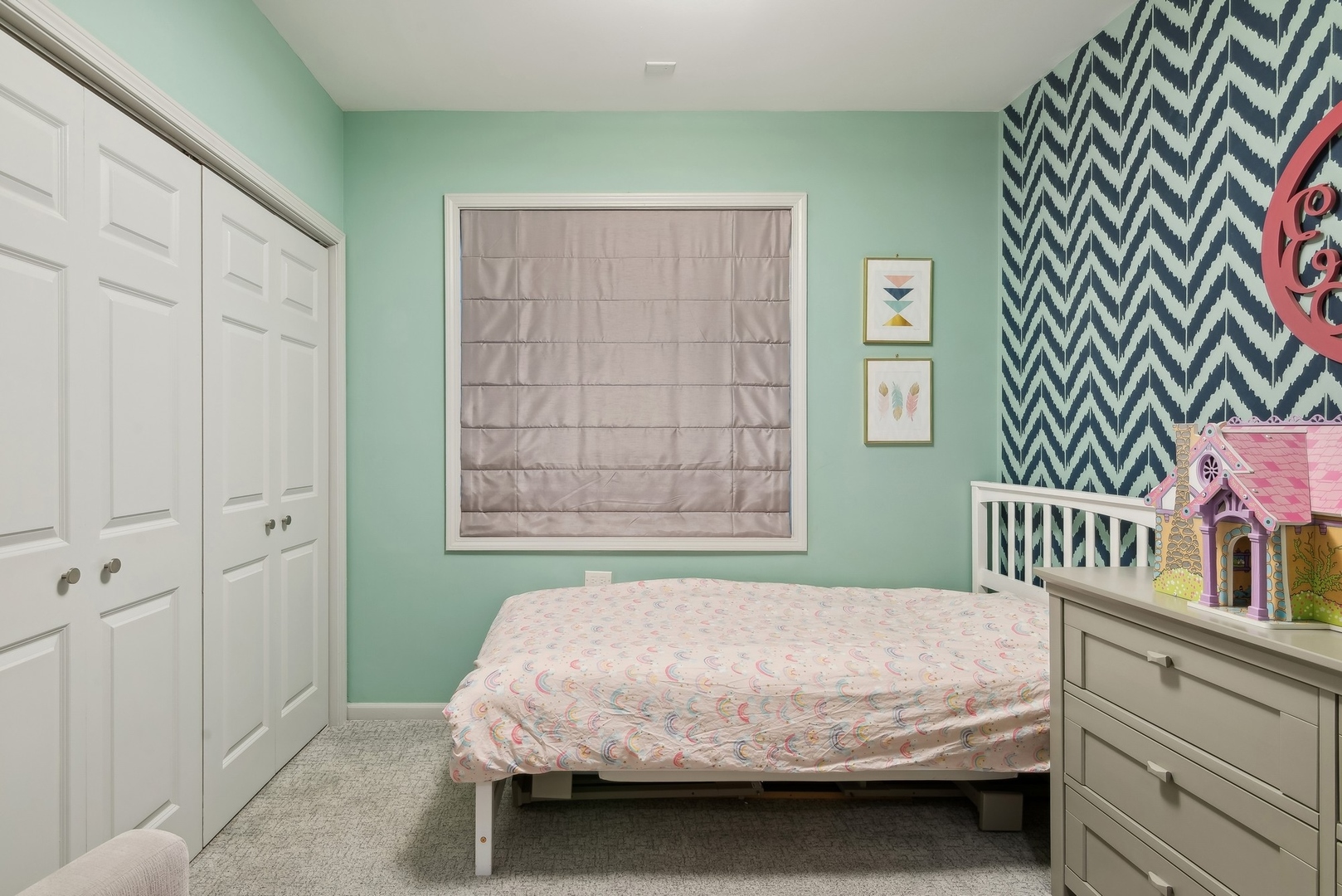 Bedroom with mint green walls, white closets, a pastel rainbow-print bedspread, and a navy chevron accent wall.