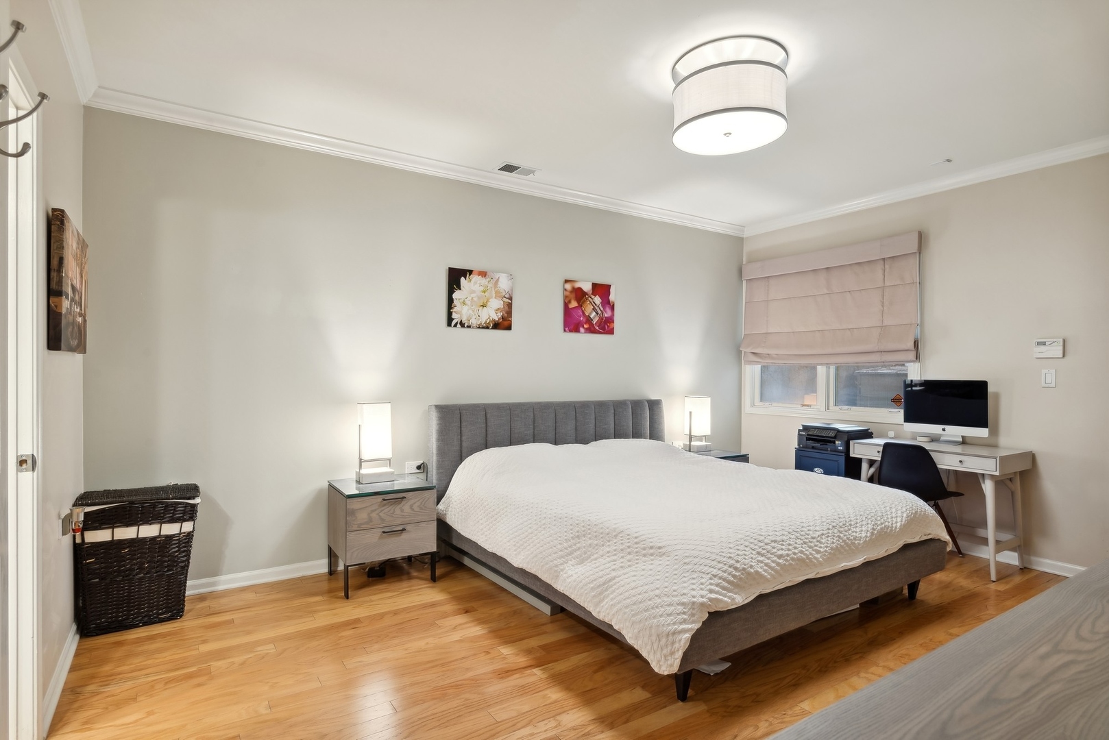 Furnished bedroom with a large gray bed, hardwood floors, and a desk beside the window.