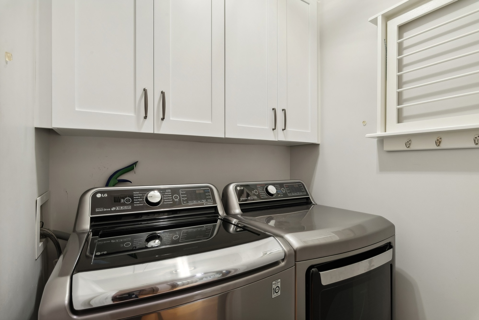 Laundry room with stainless steel washer and dryer beneath white cabinets and beside a wall-mounted rack.