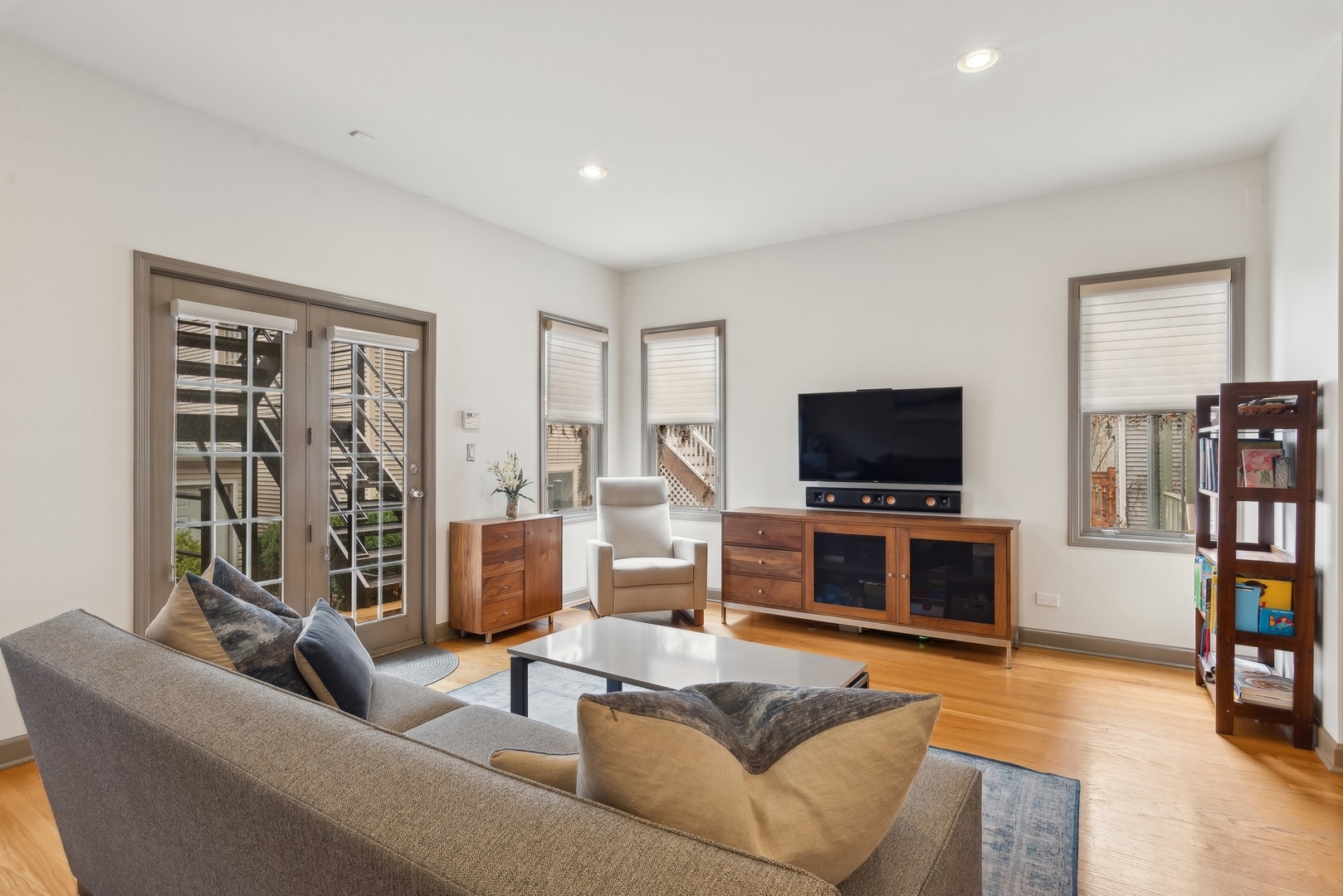 Living room with hardwood floors, a gray sectional, and French doors opening to an outdoor area.