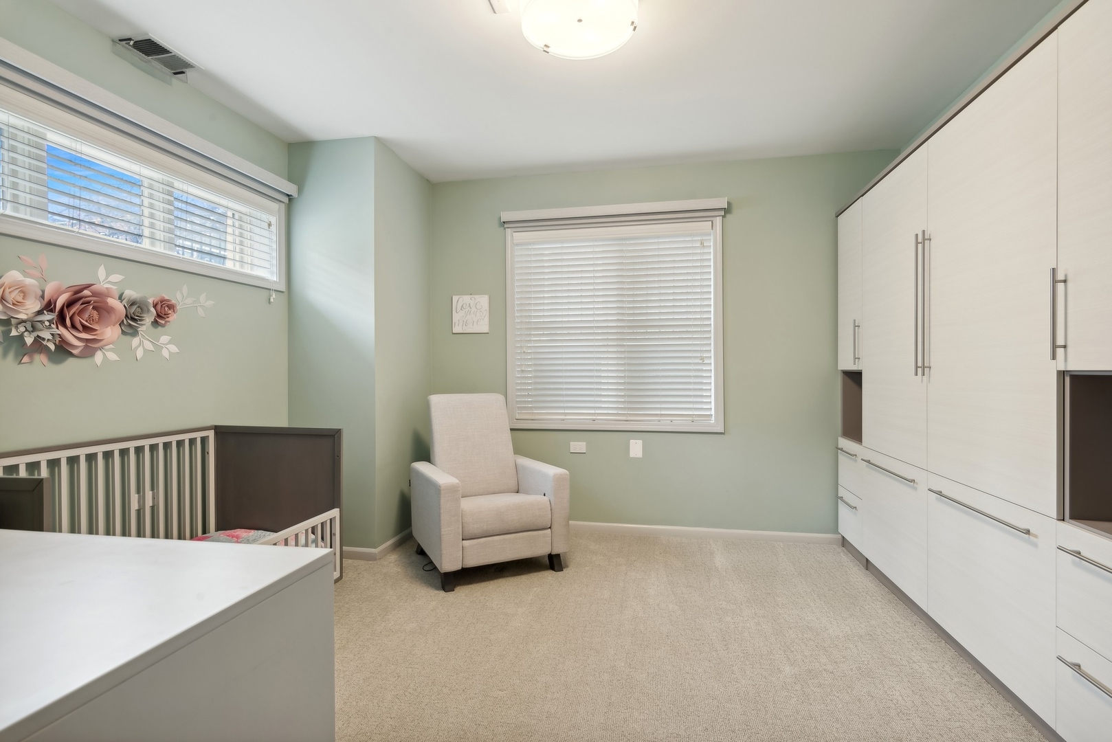 Nursery with a crib, beige armchair, pale green walls, and white built-in cabinets.