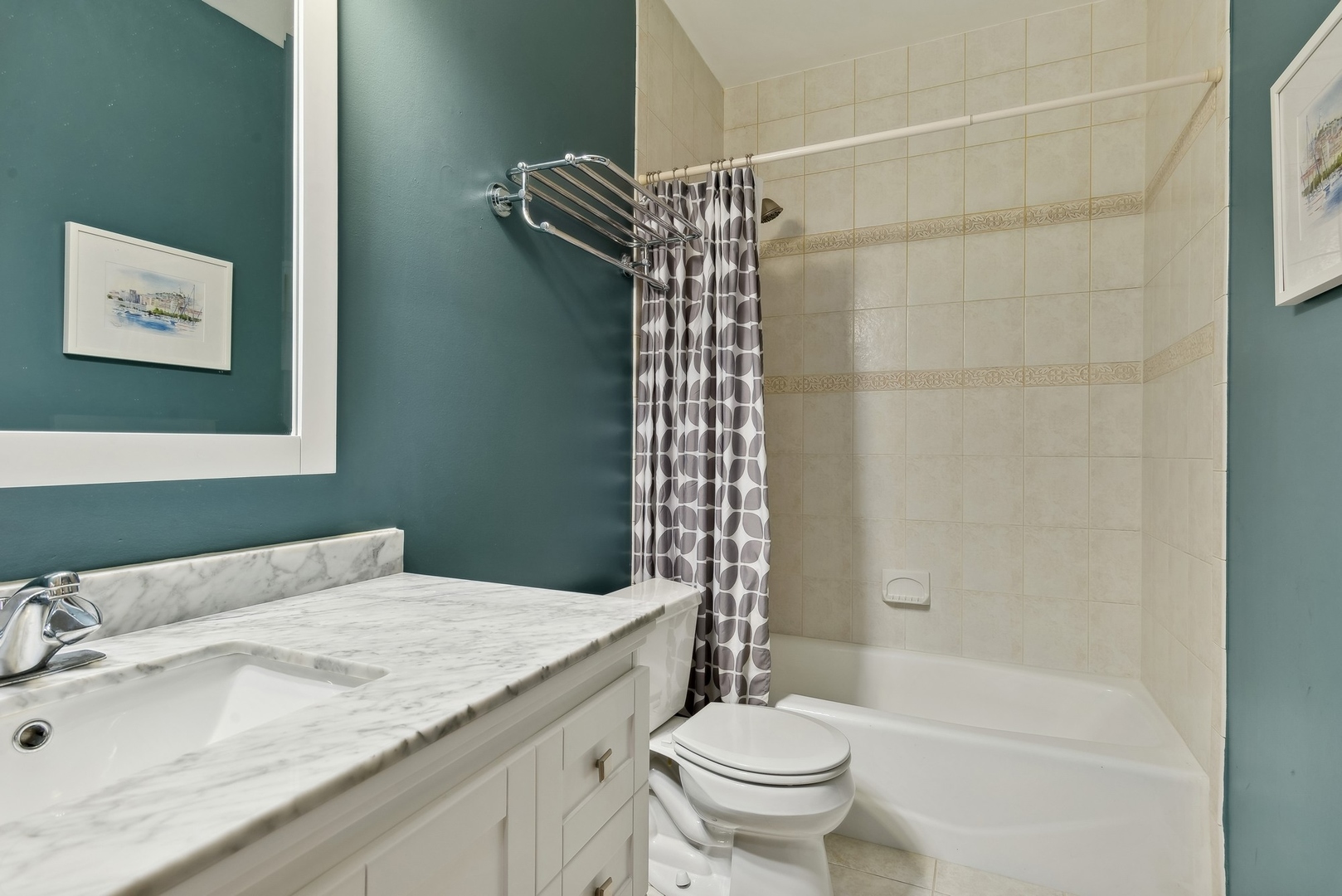 Bathroom with marble-look vanity, teal walls, and a tiled tub-shower with patterned curtain.