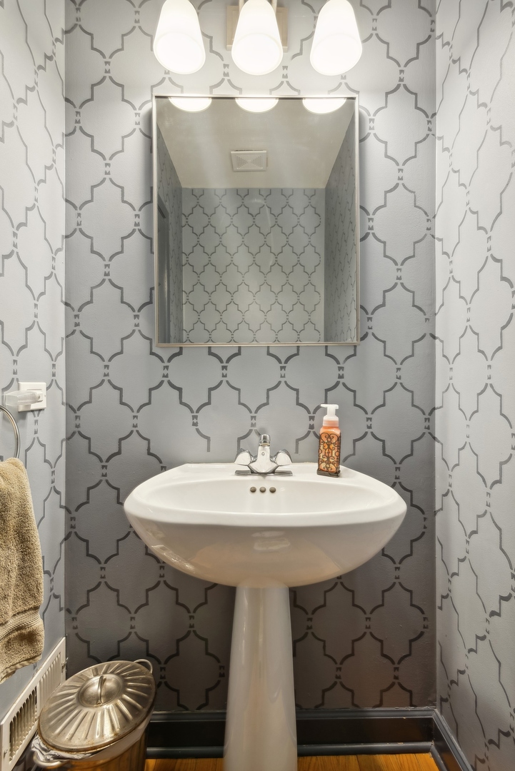 Bathroom with a white pedestal sink, rectangular mirror, and gray geometric-patterned wallpaper.