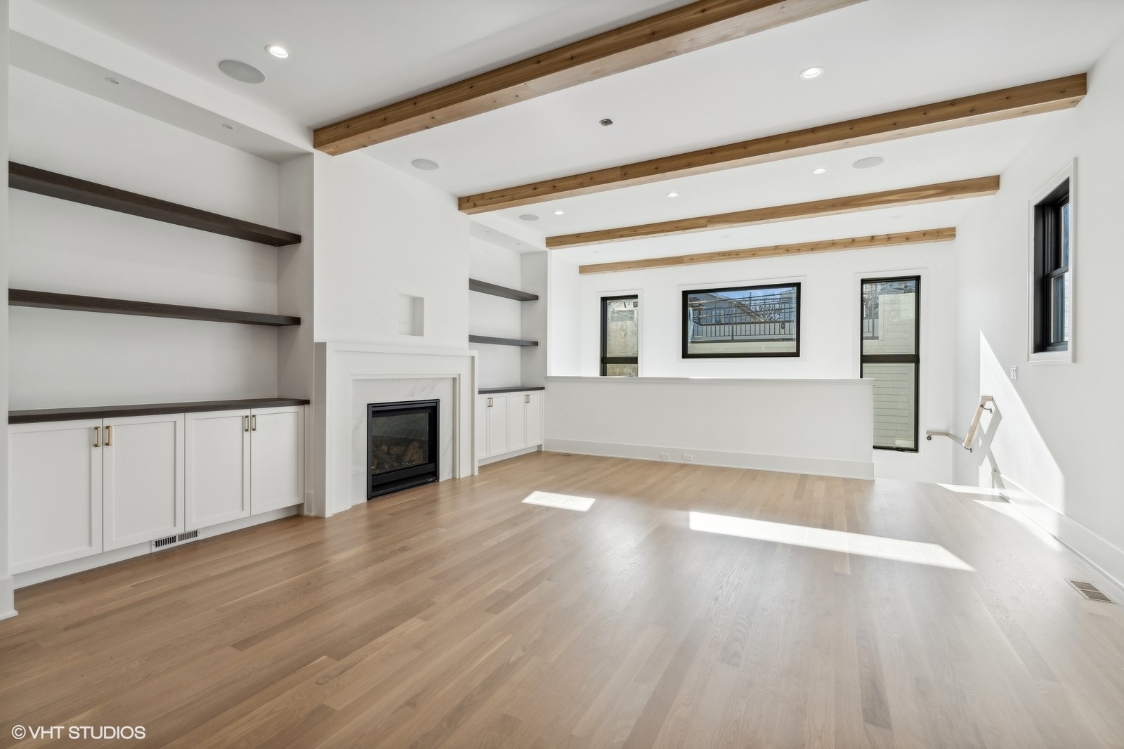 Vacant living room with exposed wood ceiling beams, built-in shelving, and a white fireplace.
