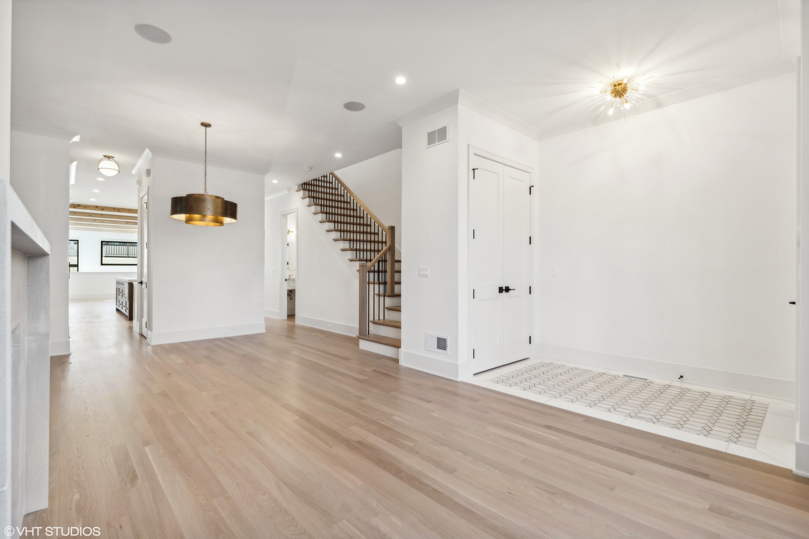 Open living area with hardwood floors, a staircase, and a patterned tile fireplace hearth.