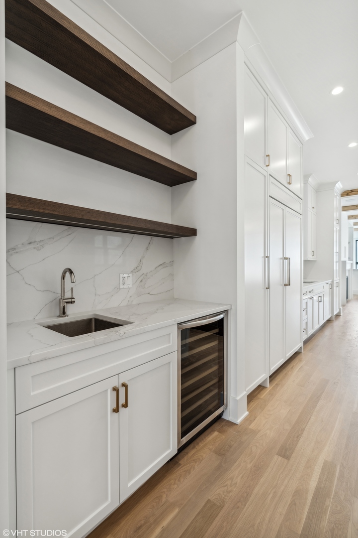 Kitchen with white cabinetry, marble-look counters, dark floating shelves, and a built-in wine refrigerator.