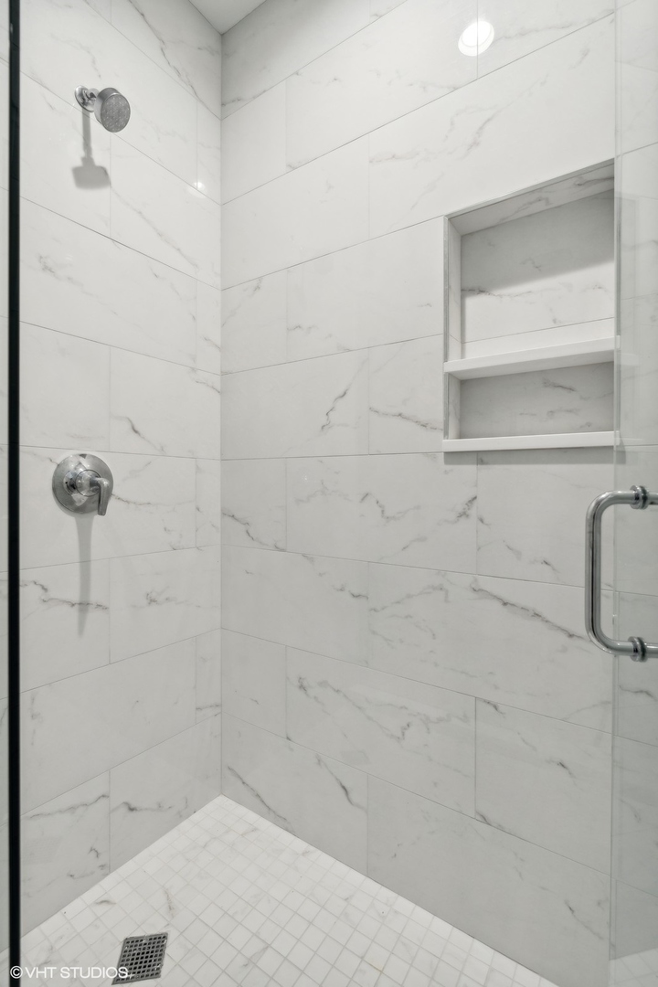 Walk-in shower with marble-look tile, recessed shelves, chrome fixtures, and a square mosaic floor.