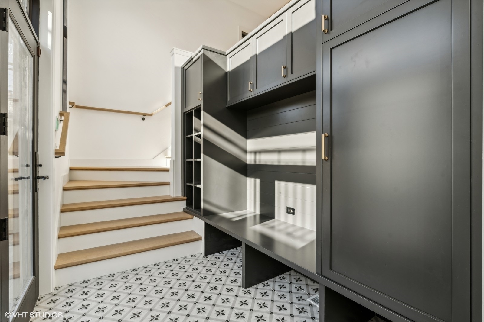 Entryway with wood-tread stairs, dark built-in cabinetry, a bench, and patterned tile flooring.