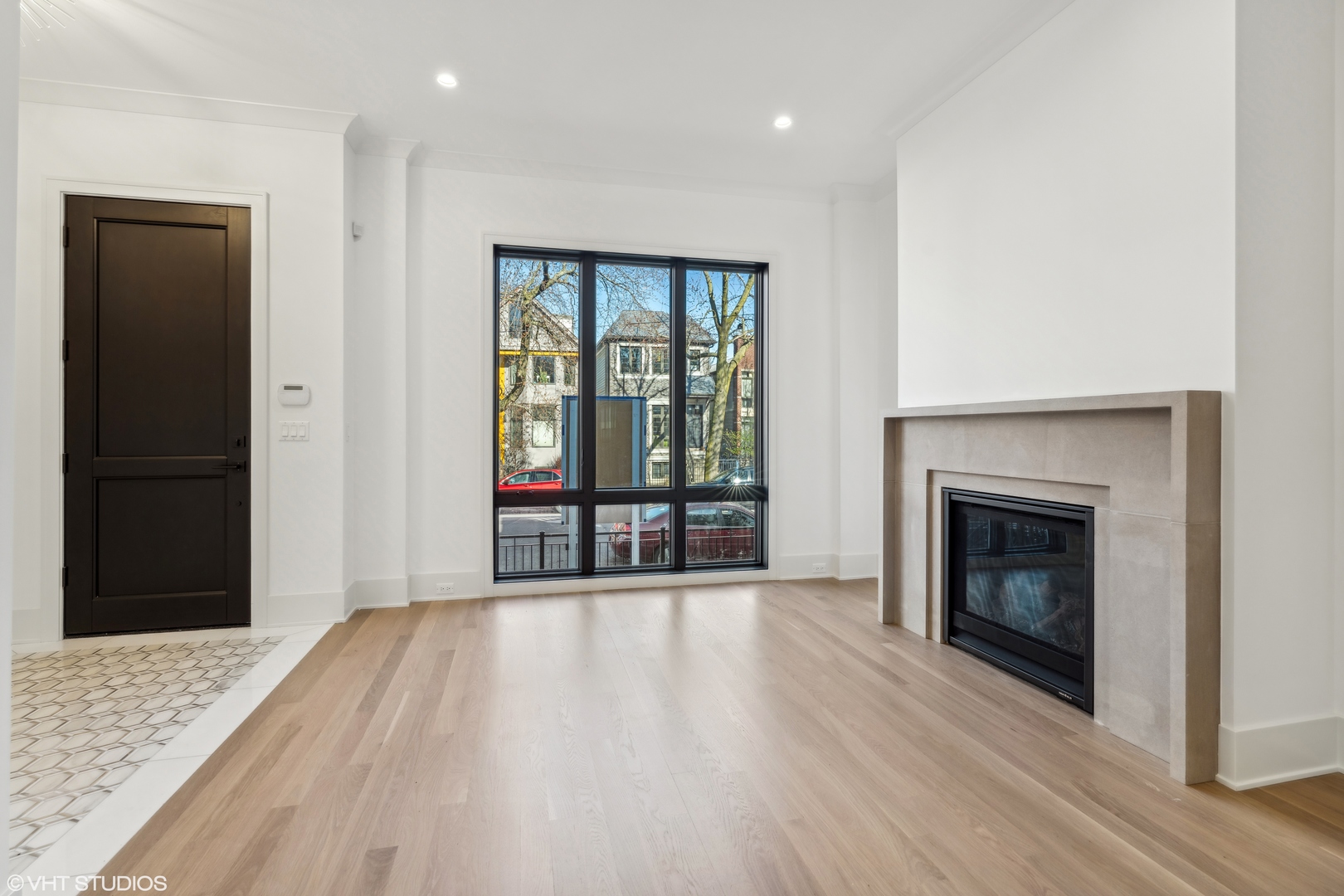 Unfurnished living room with pale wood floors, a large window, and a modern stone fireplace.
