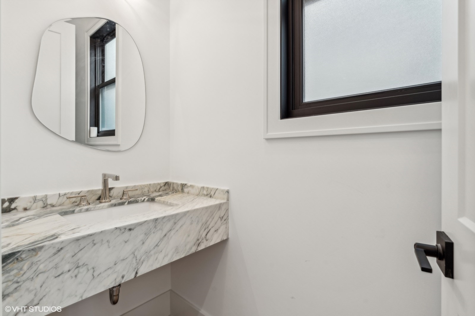 Bathroom with a floating marble vanity, wall-mounted faucet, rounded mirror, and dark-framed window.