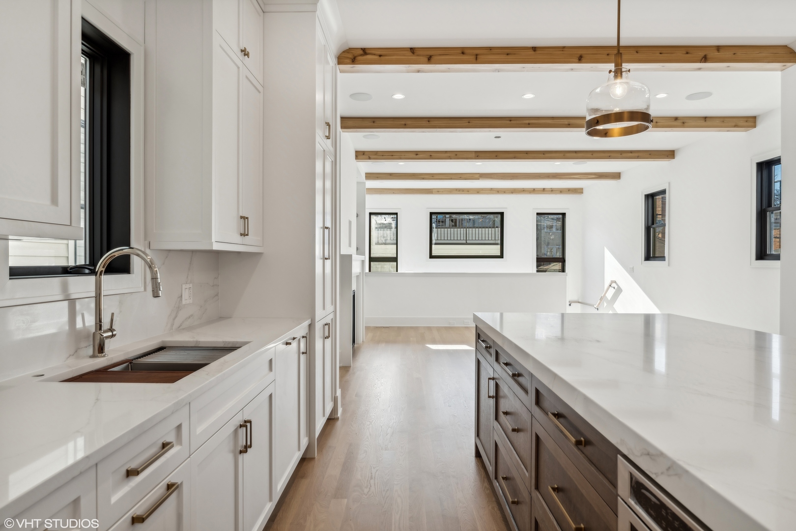 Kitchen with a large island, white cabinetry, exposed wood beams, and an open living area.