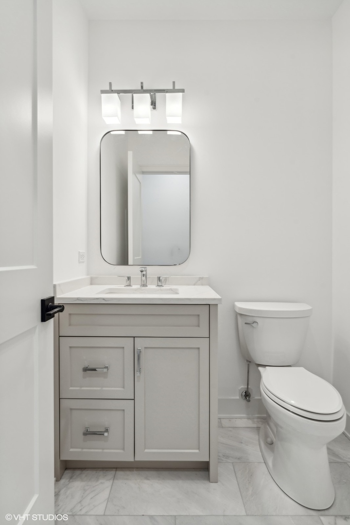 Bathroom with a gray paneled vanity, rounded mirror, and marble-look tile floor.