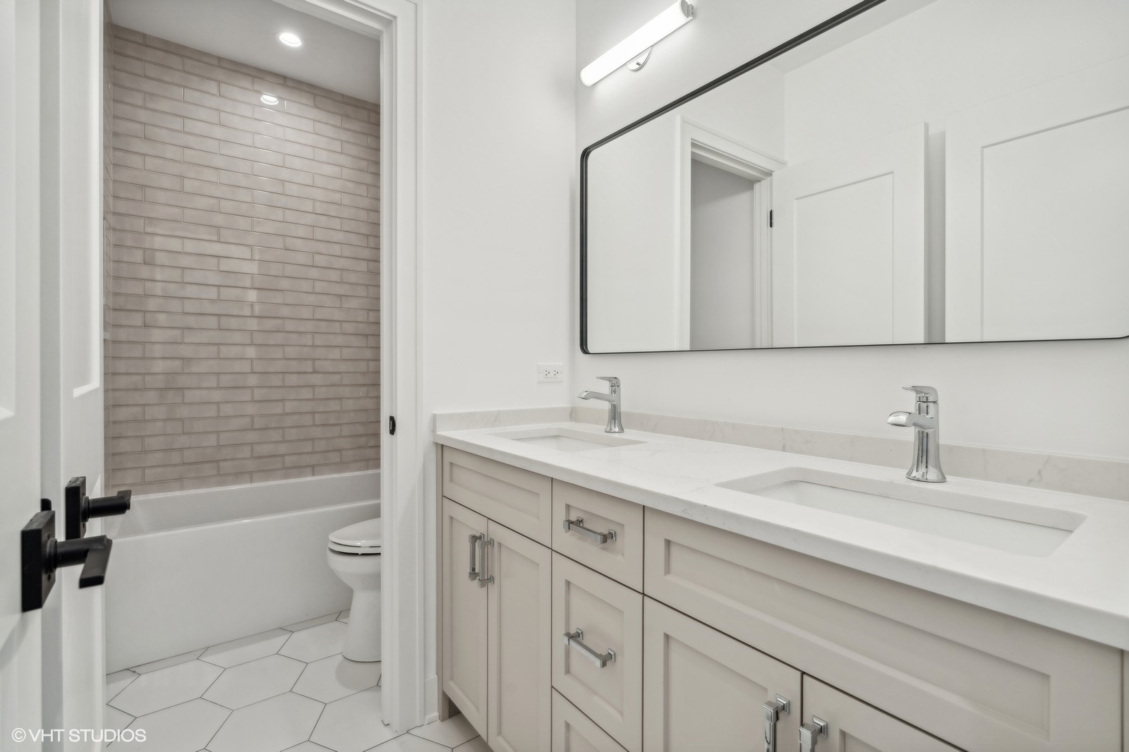 Modern bathroom with double vanity and a bathtub lined with gray subway tile.