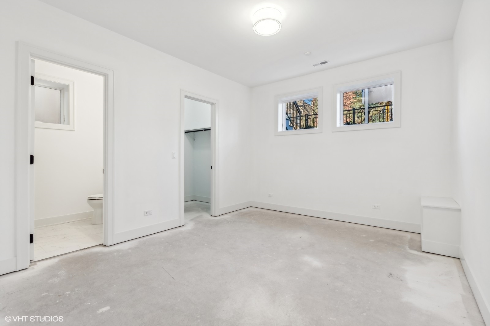Vacant white bedroom with two high windows, an open closet, and an adjoining bathroom.