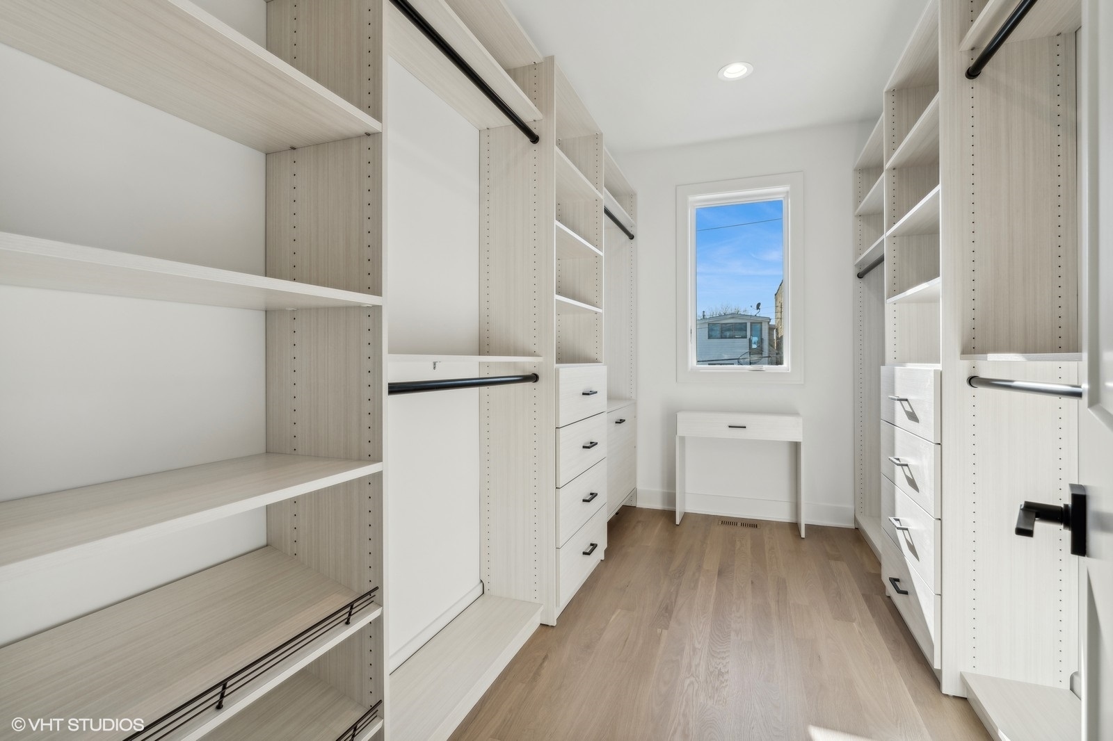 Walk-in closet with white built-in shelving and drawers, light wood floors, and a window.