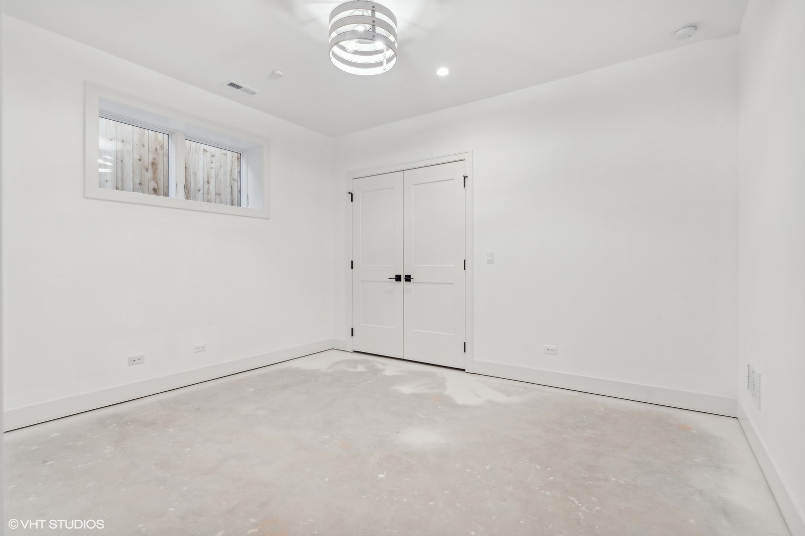 Empty room with a bare concrete floor, high-set window, white double doors, and modern ceiling light.