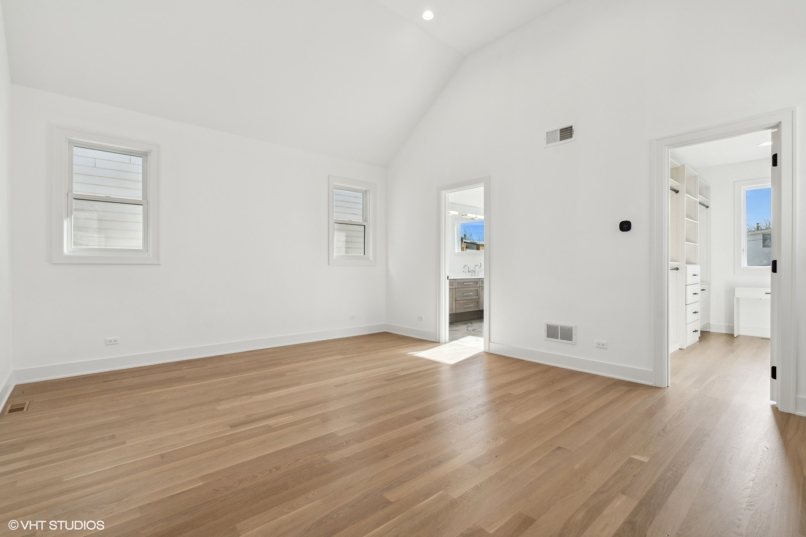 Vacant bedroom with vaulted ceiling, light hardwood floors, and doorways to a bathroom and built-in closet.