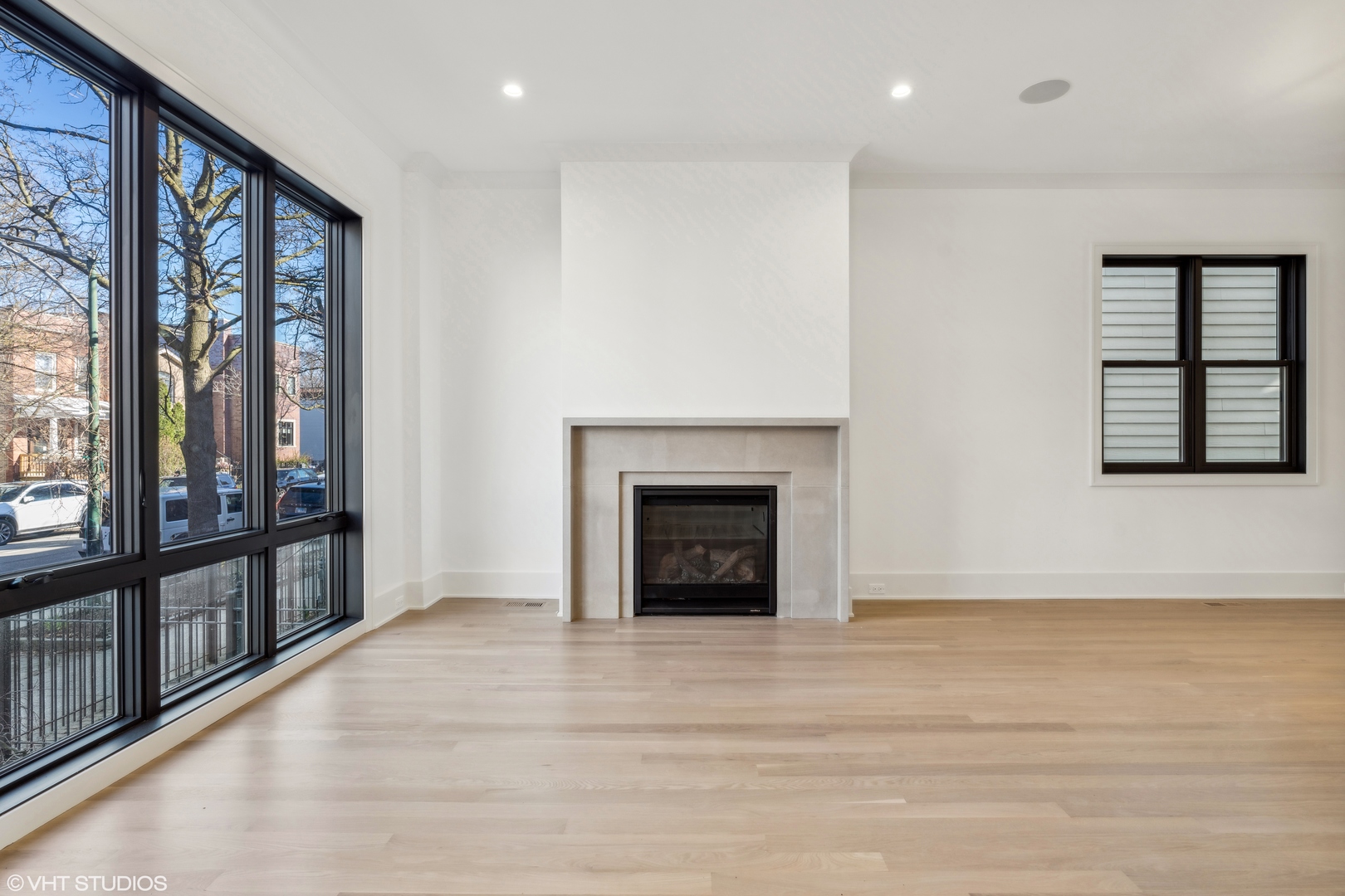 Vacant living room with a stone-surround fireplace and expansive black-framed windows.