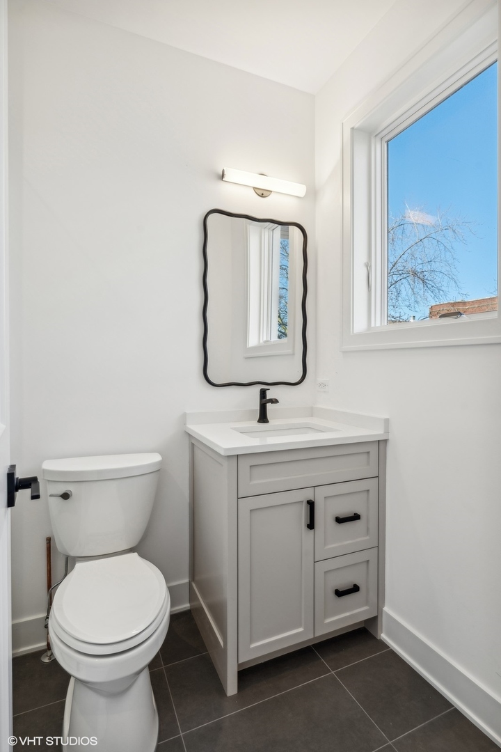 Bathroom with a gray vanity, wavy-edged mirror, white toilet, and large window.