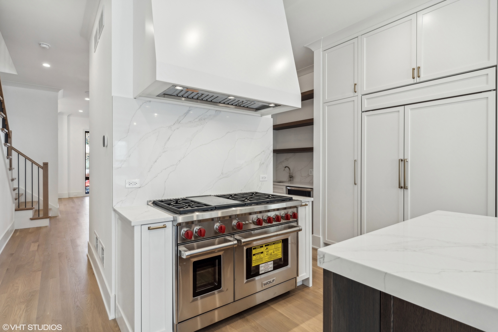 Kitchen with a stainless steel Wolf range, marble backsplash, white cabinetry, and dark wood island.