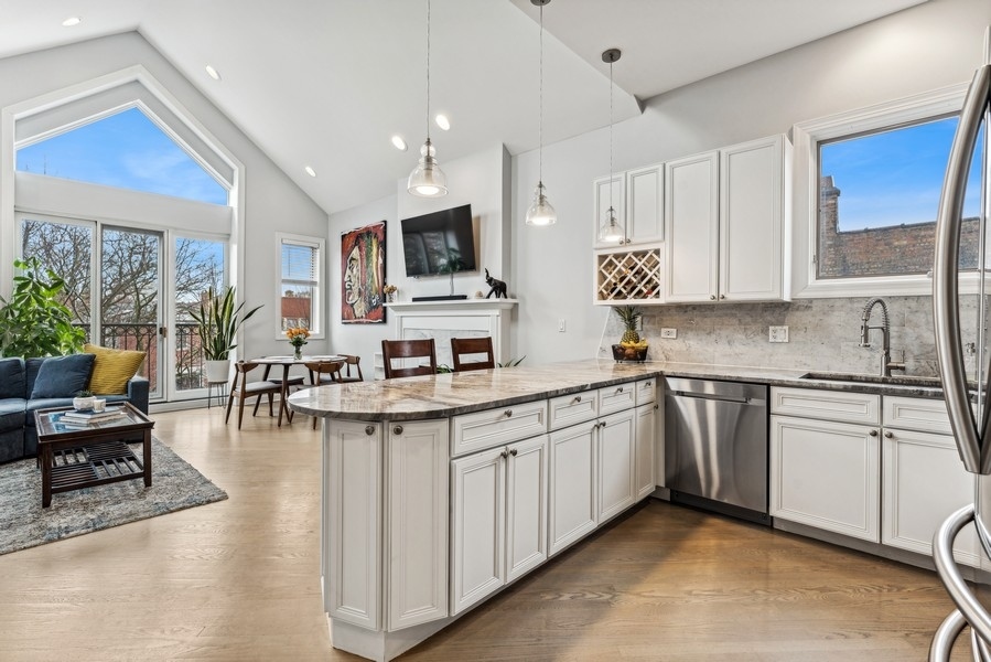 Open-plan condo kitchen with a large stone island, white cabinets, and tall windows beside the living area.