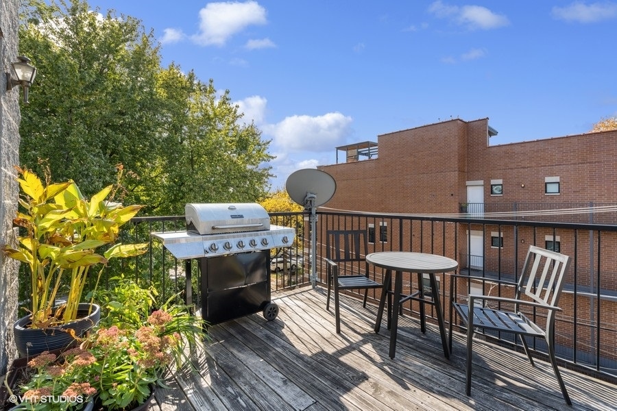 Outdoor deck with a stainless steel grill, patio table and chairs, and leafy potted plants.