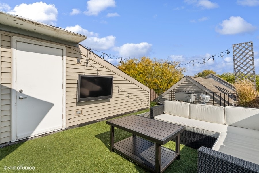 Rooftop terrace with white outdoor sectional, artificial turf, wall-mounted television, and string lights.