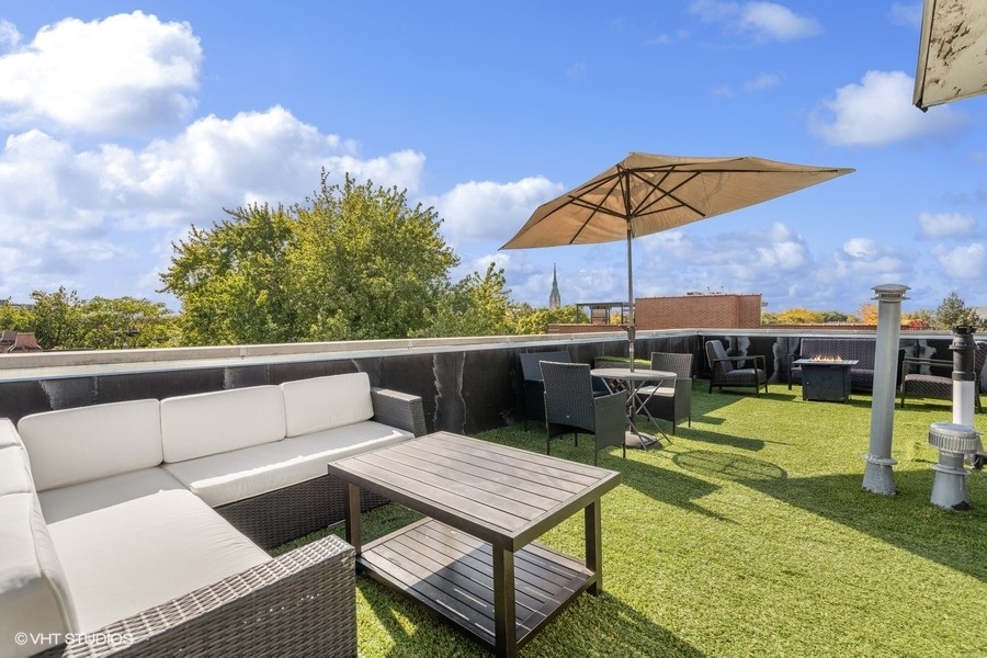 Rooftop terrace with artificial grass, wicker sectional seating, and a large beige umbrella.