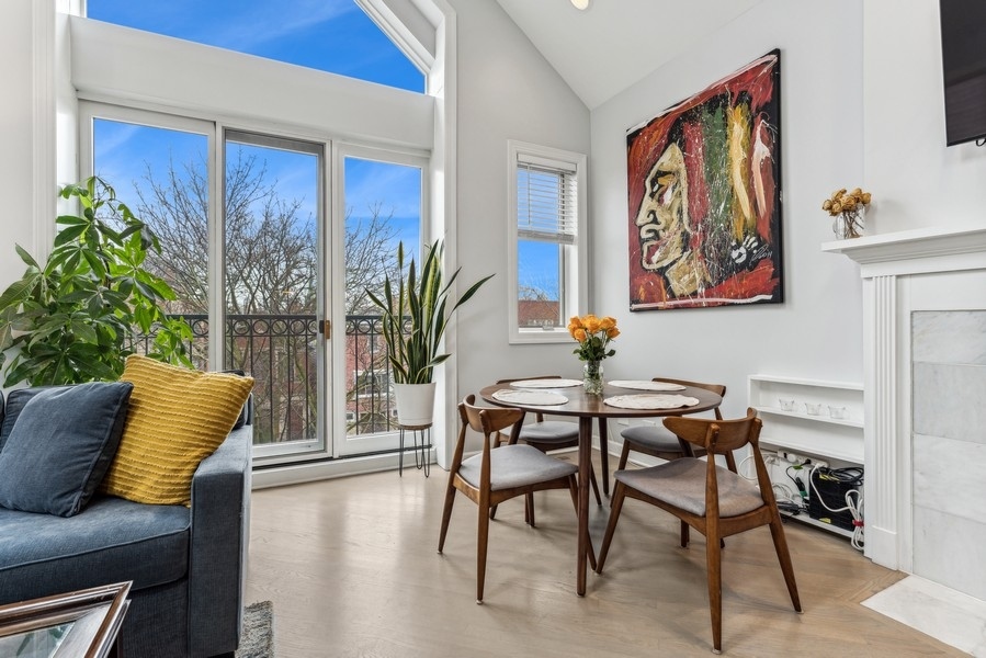 Living and dining area with tall balcony windows, a blue sofa, and a round wood dining table.