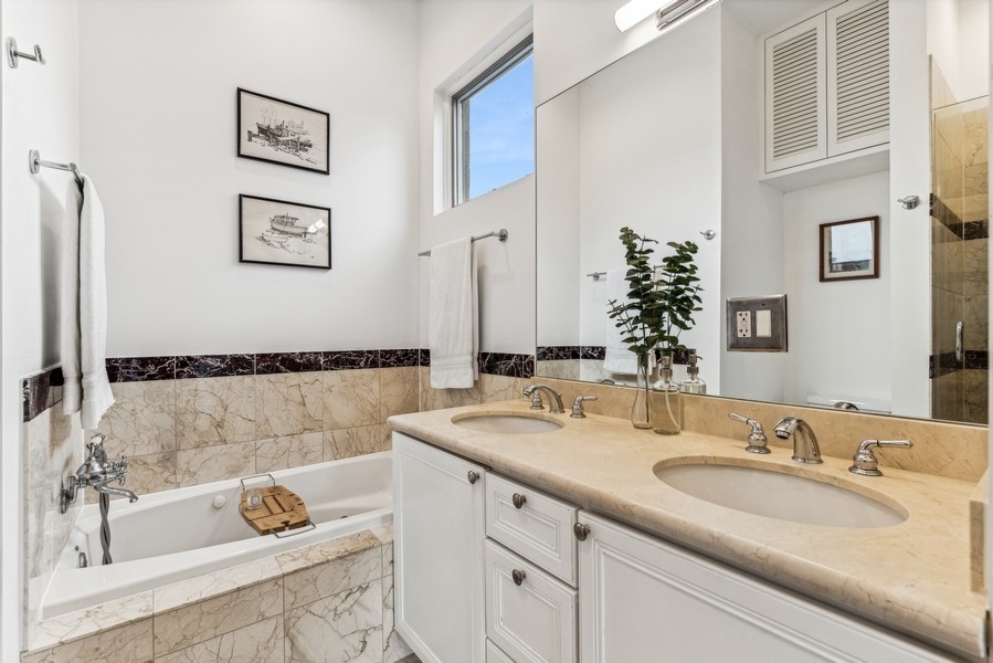 Bathroom with a white bathtub and double vanity topped with beige marble.
