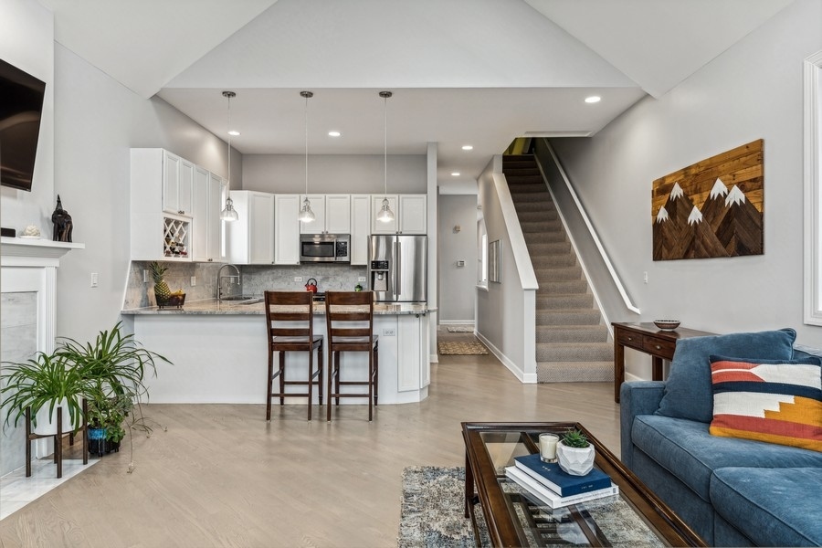 Open-plan living room and kitchen with white cabinetry, a breakfast bar, and staircase beside a blue sofa.