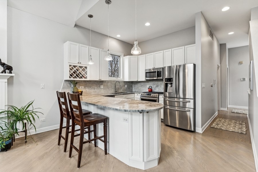 Kitchen with a stone-topped island, two wooden stools, white cabinetry, and stainless steel appliances.