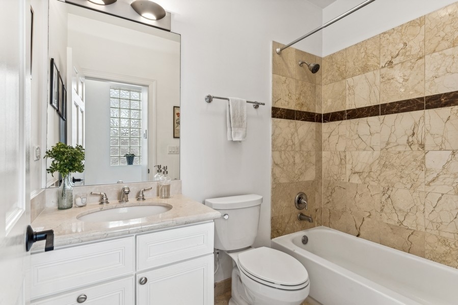 Bathroom with white vanity and tub featuring beige marble tile and a dark accent band.