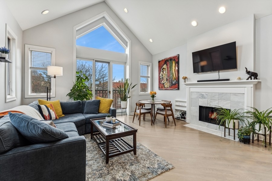 Living room with a vaulted ceiling, tall windows, sectional sofa, and marble fireplace.