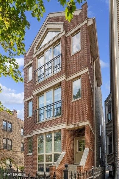 Red-brick residential building with black-railed balconies and a recessed entrance, viewed from the street.