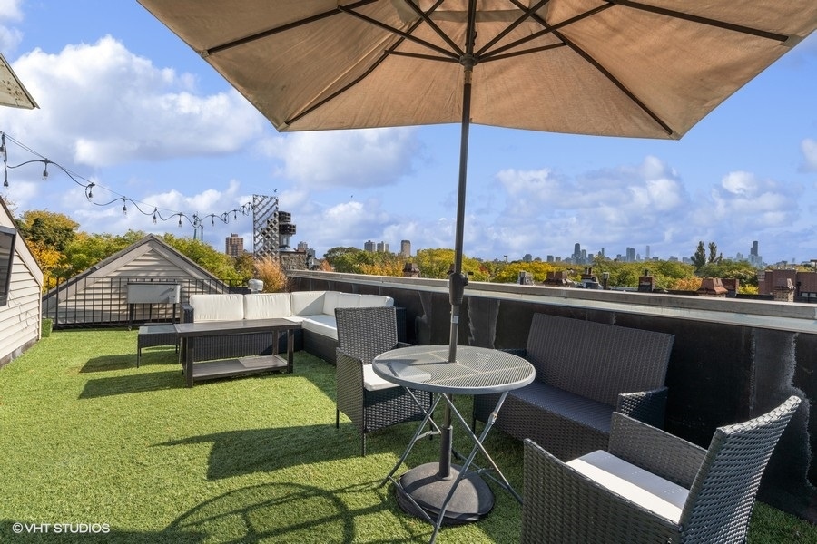 Rooftop deck with wicker seating and umbrella, overlooking trees and the Chicago skyline.