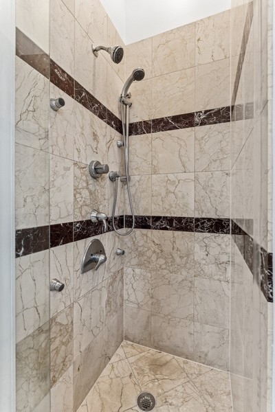 Walk-in tiled shower with multiple chrome showerheads and dark marble accent bands.