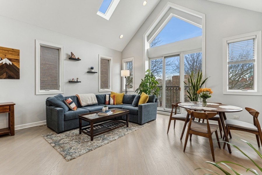 Living and dining room with a dark sectional, vaulted ceiling, skylight, and tall windows.