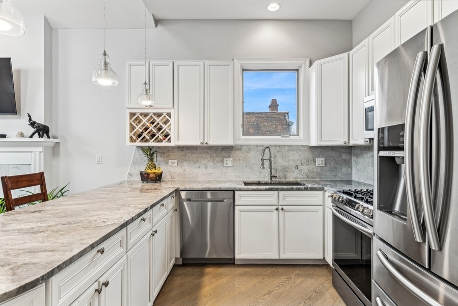 Kitchen with white cabinetry, marble counters, stainless steel appliances, and a broad peninsula.
