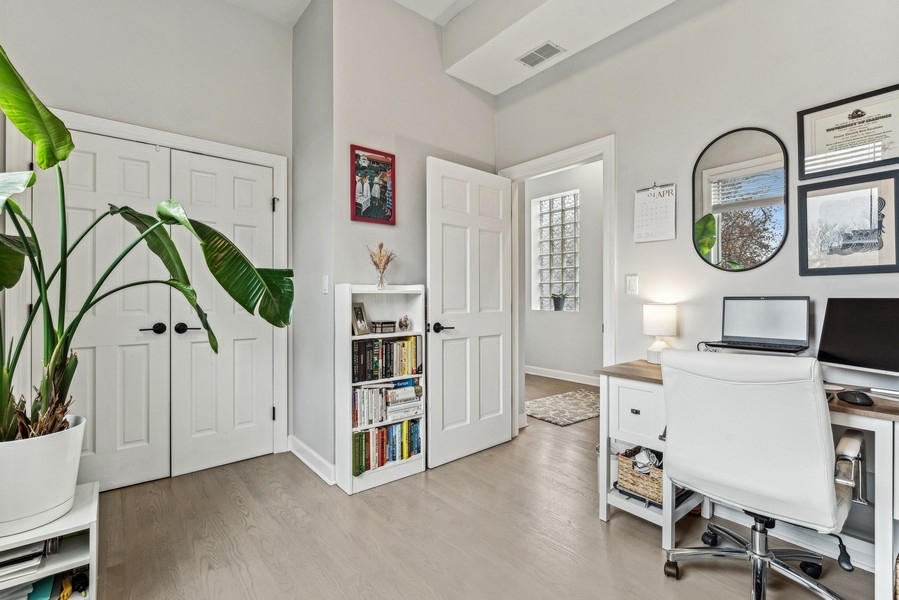 Furnished home office with a white desk, glass-block window, and large potted plant.