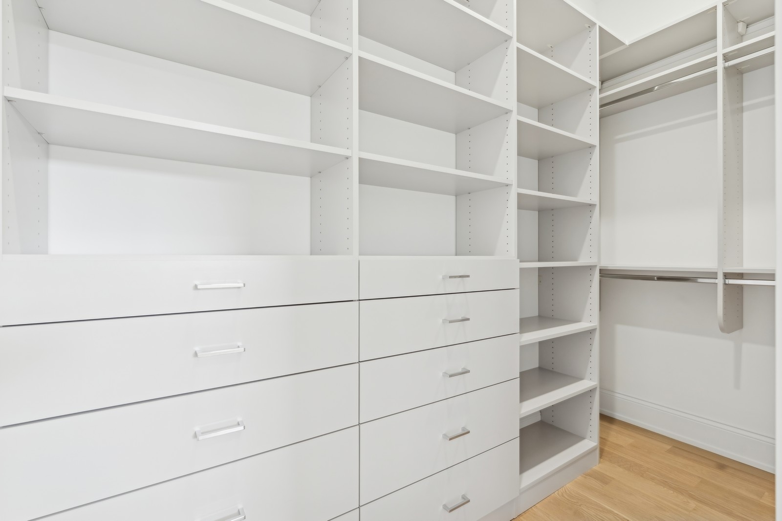 Walk-in closet with white built-in drawers, shelving, and hanging rods.