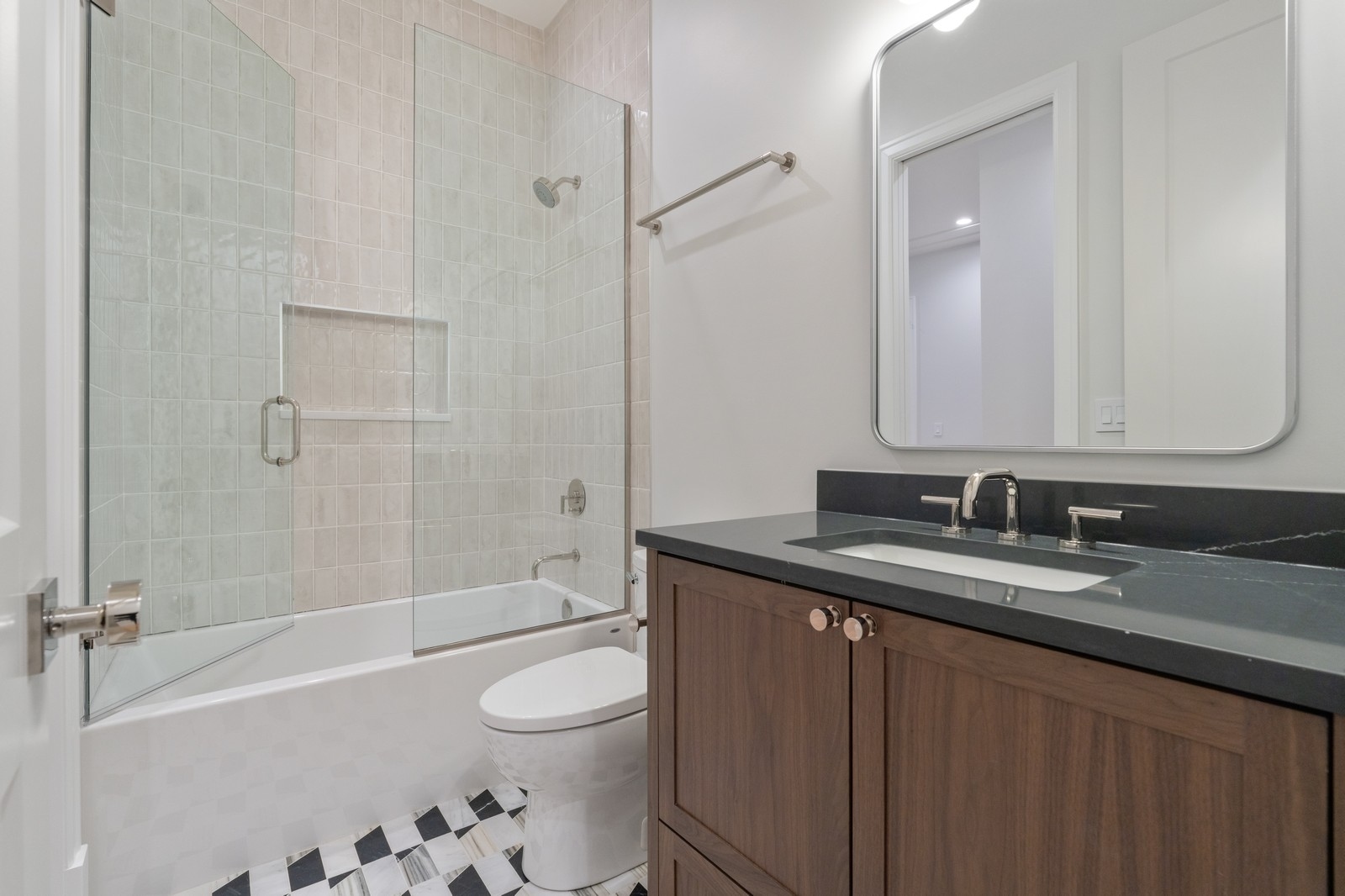Bathroom with a glass-enclosed tub and shower, dark countertop, wood vanity, and patterned floor tiles.