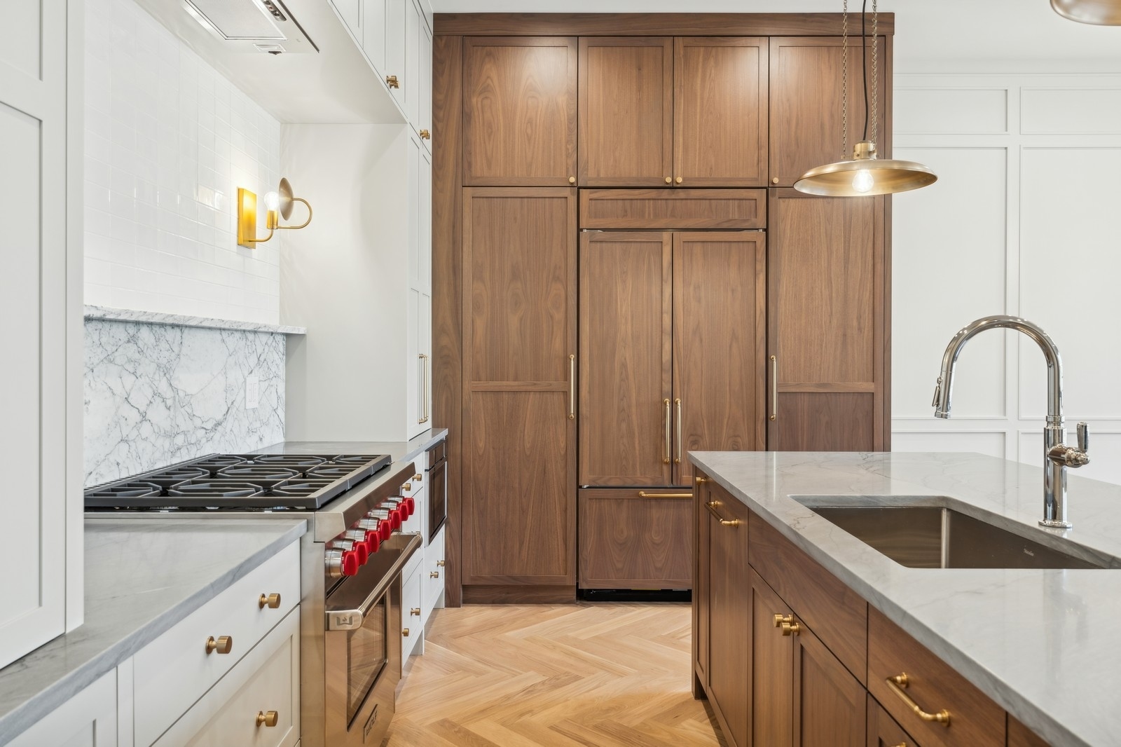Kitchen with walnut cabinetry, marble counters, a red-knob gas range, and a large island sink.