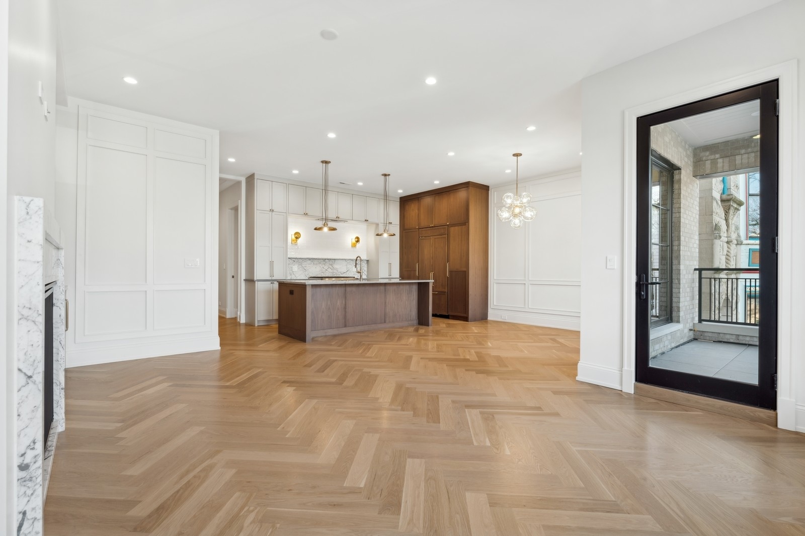 Open-plan kitchen with dark wood island, white cabinetry, herringbone floors, and a balcony door.