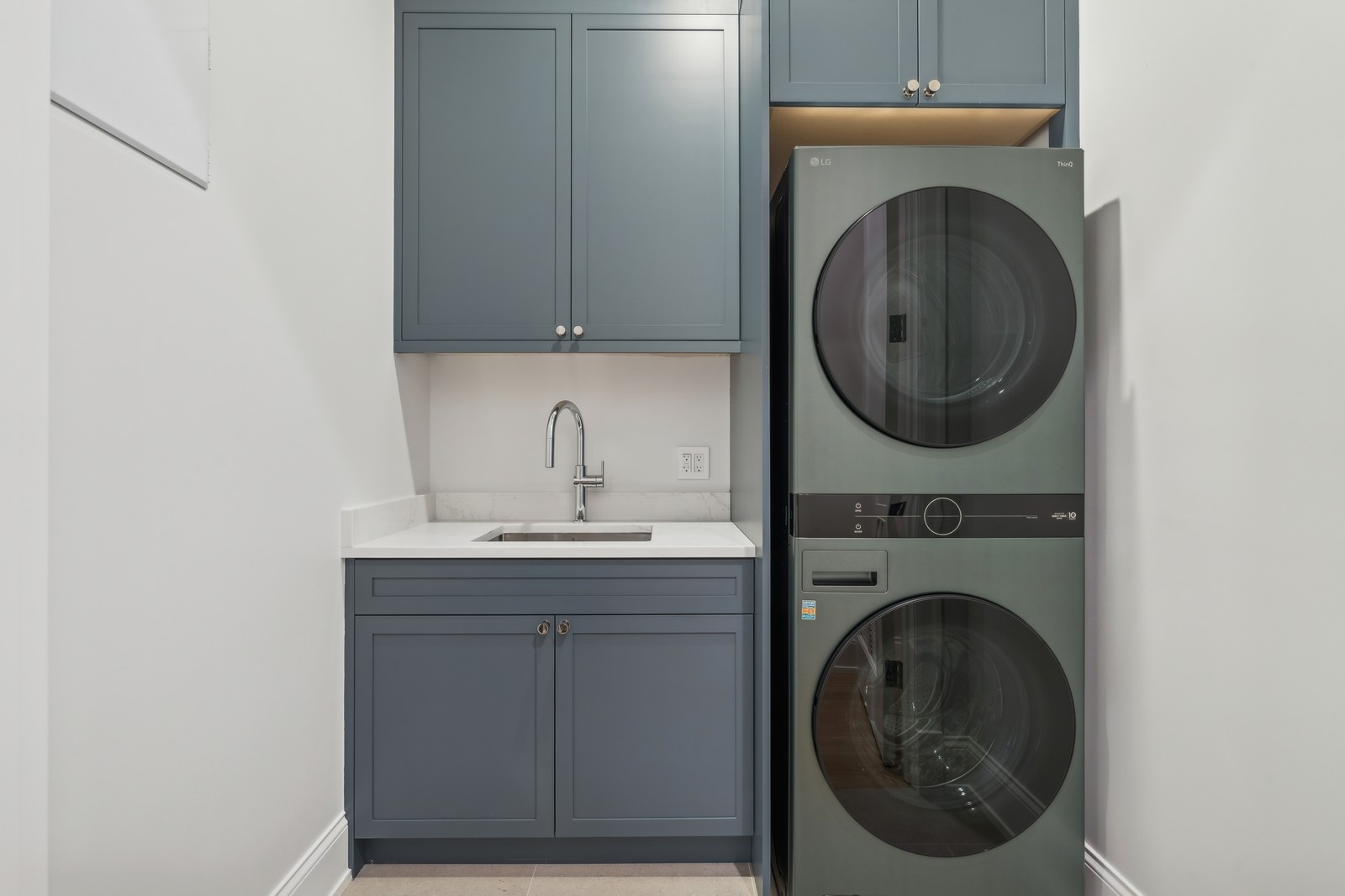 Laundry room with slate-blue cabinetry, a sink, and a stacked washer and dryer.